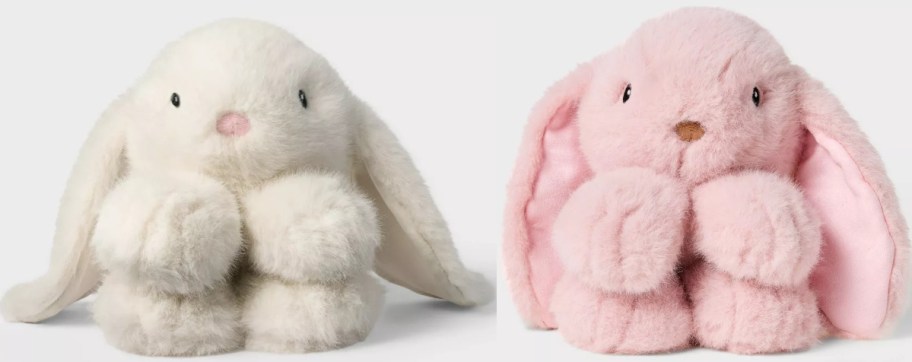 Two plush bunnies are sitting side by side. The bunny on the left is white with pink accents, while the bunny on the right is pink with beige accents. Both have large floppy ears.