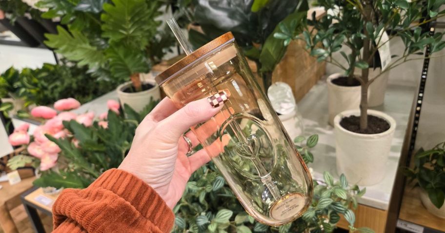 hand holding heart tumbler in front of greenery
