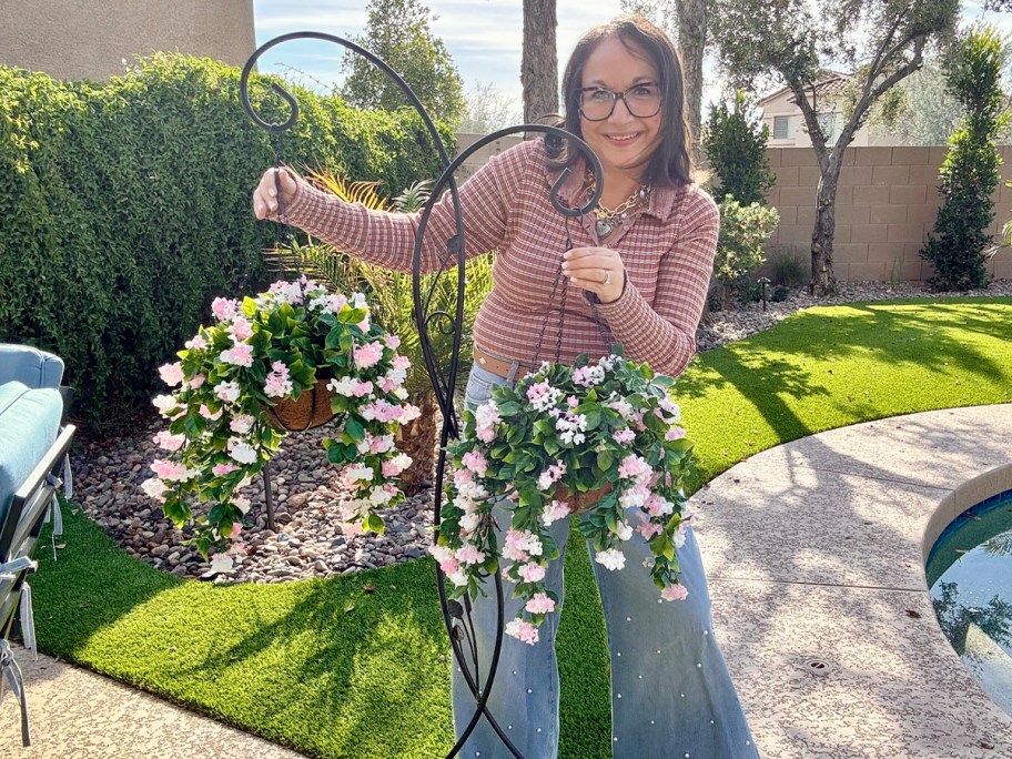 woman standing behind two hanging pink floral baskets 