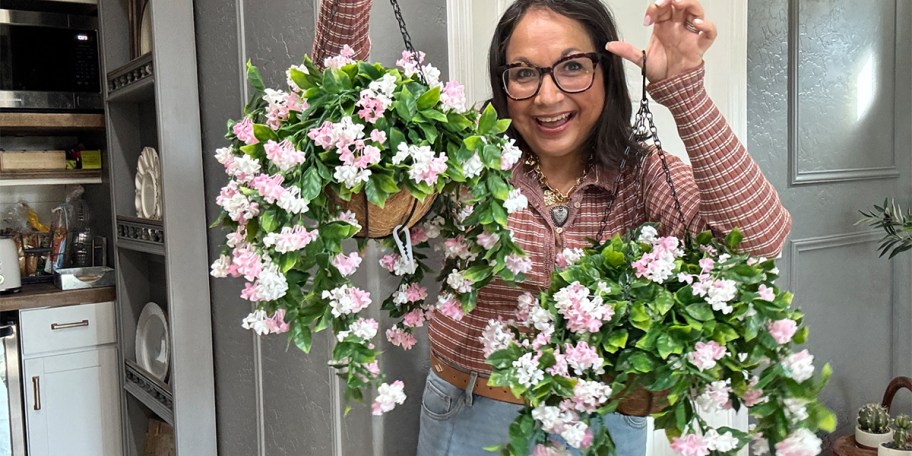 woman holding two pink floral hanging baskets 