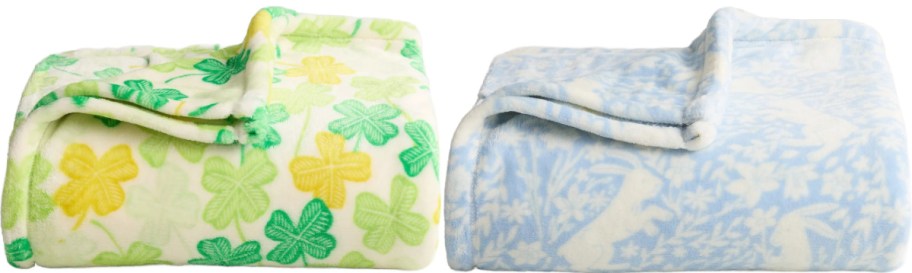 Two soft, folded blankets on display. The left is white with green and yellow shamrock patterns, while the right is light blue with white floral and bunny designs.