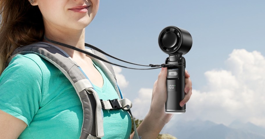 woman using a handheld fan to cool off while outdoors