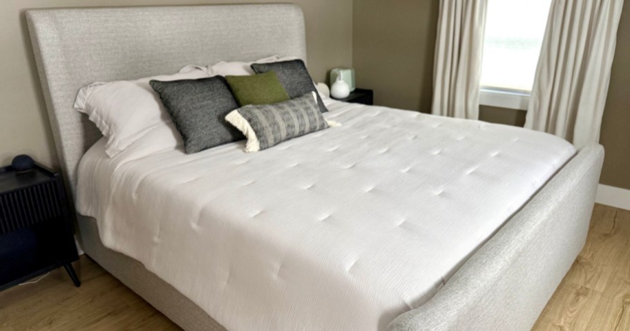 Neat bedroom with neatly made double bed with white bedding and several decorative pillows.