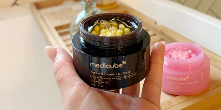 hand holding open jar of capsule cream