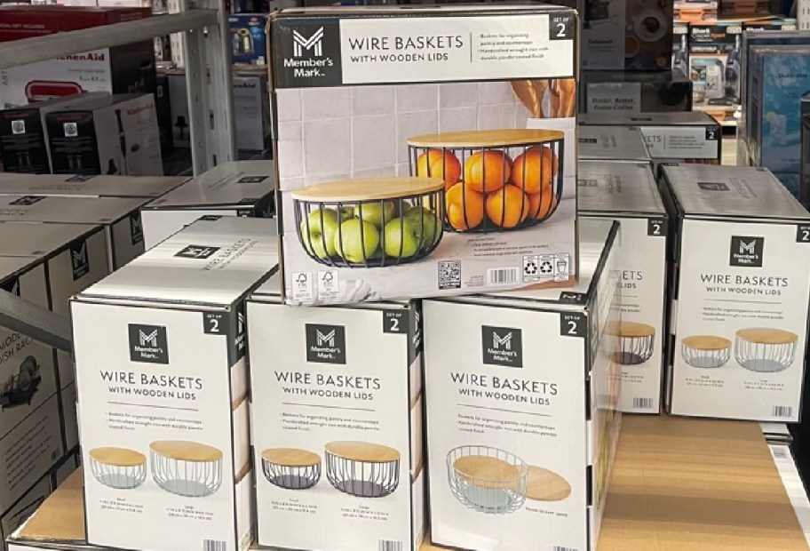 A display featuring boxes of wire baskets with wooden lids. The boxes are stacked and show pictures of the baskets filled with fruit.