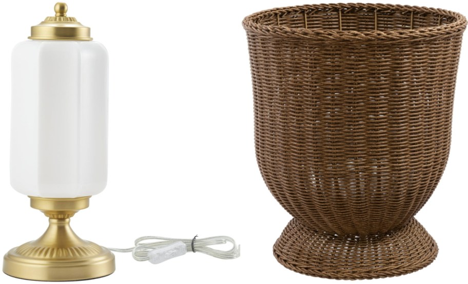 A gold lamp with a white cylindrical shade and a brown wicker basket are side by side. The lamp's cord is coiled neatly beside its base.