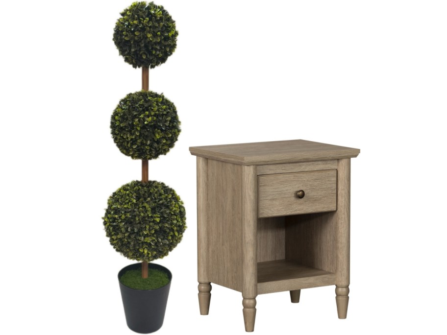 A light wooden nightstand with a single drawer next to a black pot holding a three-ball topiary plant.