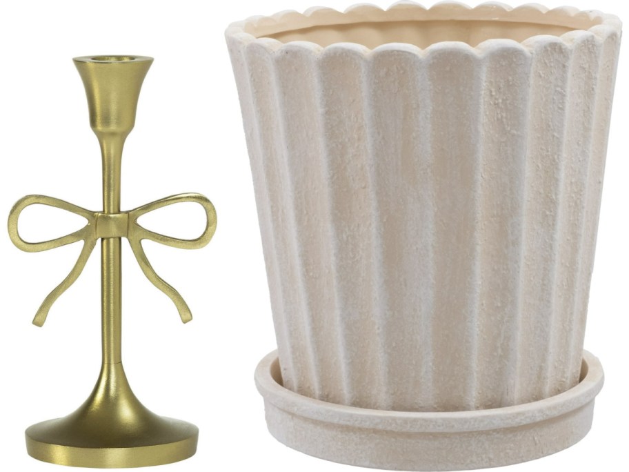 A gold candlestick with a decorative bow beside a textured, beige, fluted planter on a matching saucer.