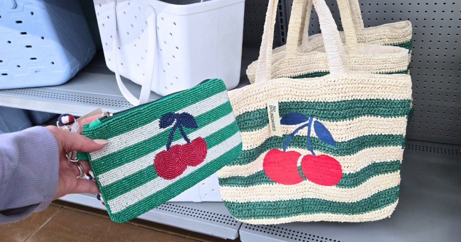 hand holding a wallet with green and white stripes and cherries next to a matching tote bag
