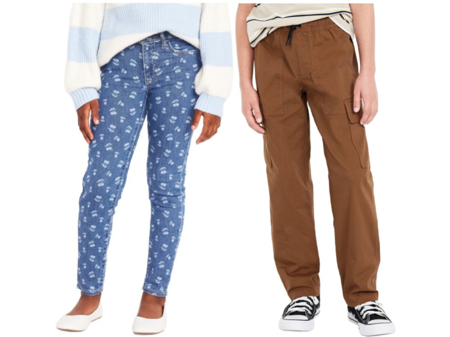 A child is wearing blue floral-patterned jeans and a striped sweater beside another in brown cargo pants and a striped t-shirt.