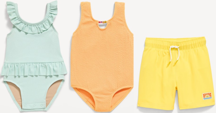 Three children's swimwear items: mint green ruffle one-piece, orange textured one-piece, and yellow shorts with white drawstring and sun logo.