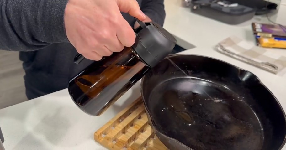 person using olive oil dispenser on a pan