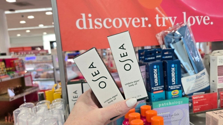 womans hand holding two body oil minis