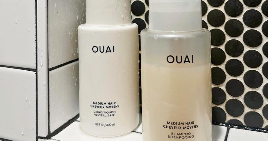 Two bottles of Ouai hair products for medium hair, positioned on a tiled bathroom shelf. One is a white conditioner, and the other is a translucent shampoo.