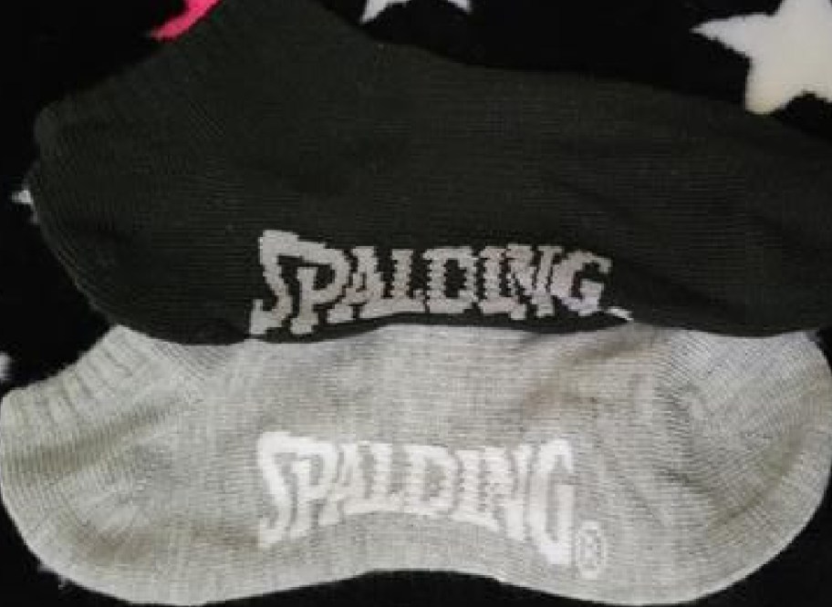 Two pairs of Spalding athletic socks stacked on top of each other, featuring one black pair and one gray pair with the Spalding logo visible.
