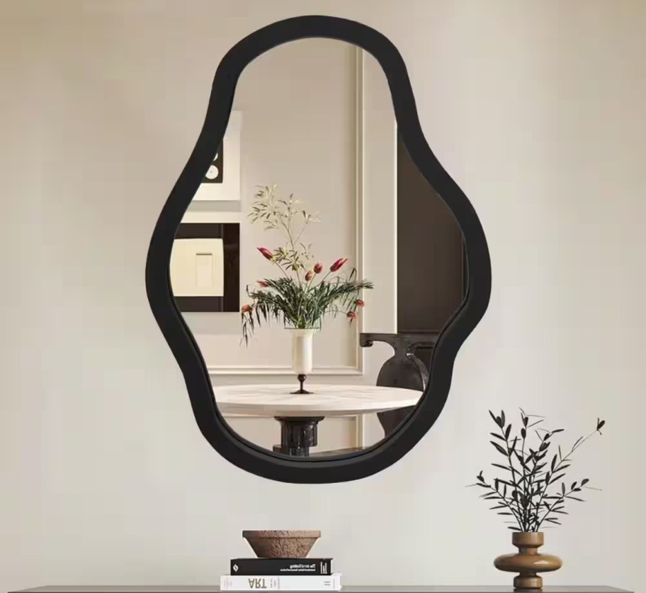 irregular wall mirror hanging above bookshelf