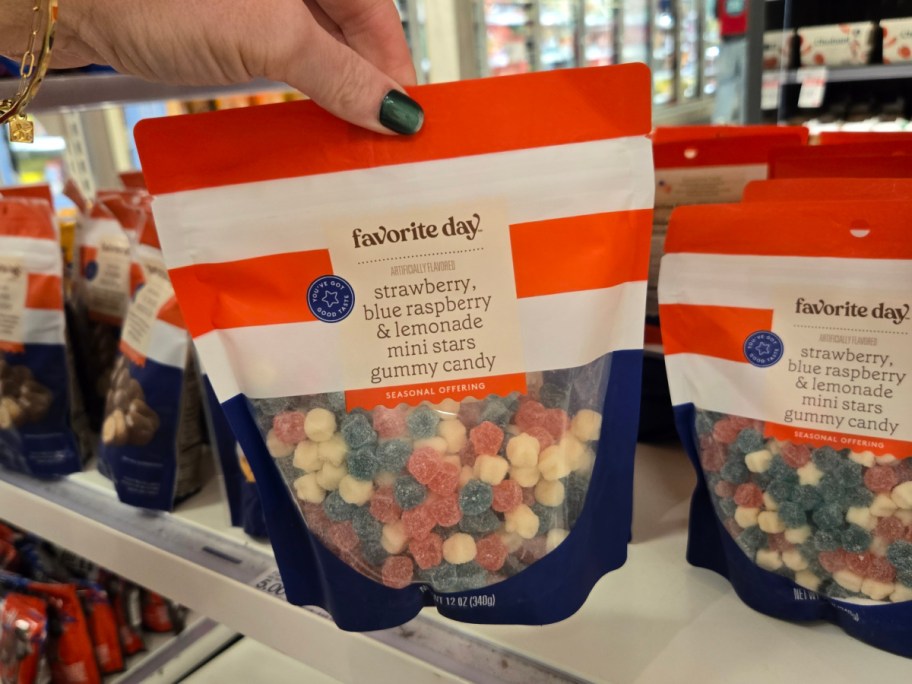A hand holds a bag of "Favorite Day" gummy candy in a store. The packaging is orange, white, and blue, displaying colorful star-shaped gummies inside.