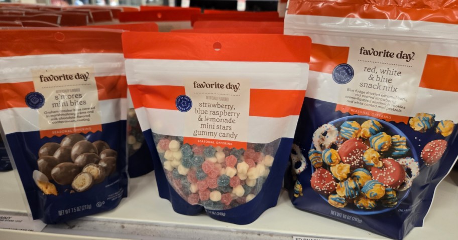Close-up of three "Favorite Day" snack bags on a store shelf. Flavors include s&rsquo;mores, fruity gummy stars, and red, white, and blue snack mix.