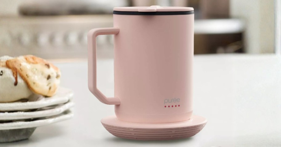 a pink self warming coffee mug next to a plate of scones