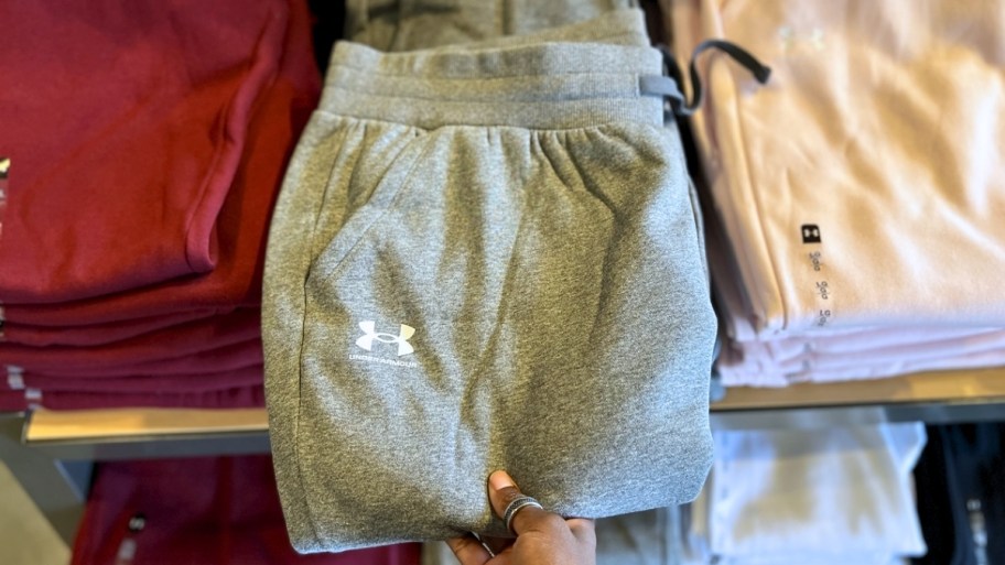 womnas hand grabbing a pair of sweatpants from a display table
