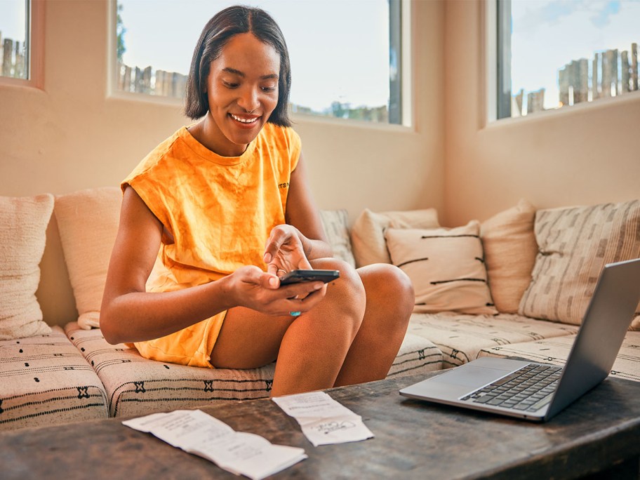 woman photographing receipts while working on her taxes on a laptop