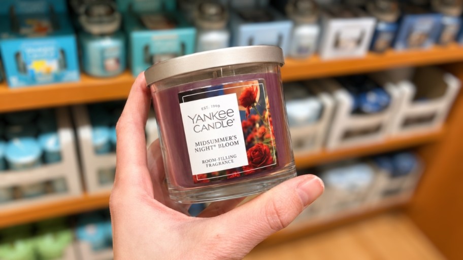 a hand holding a small jar candle