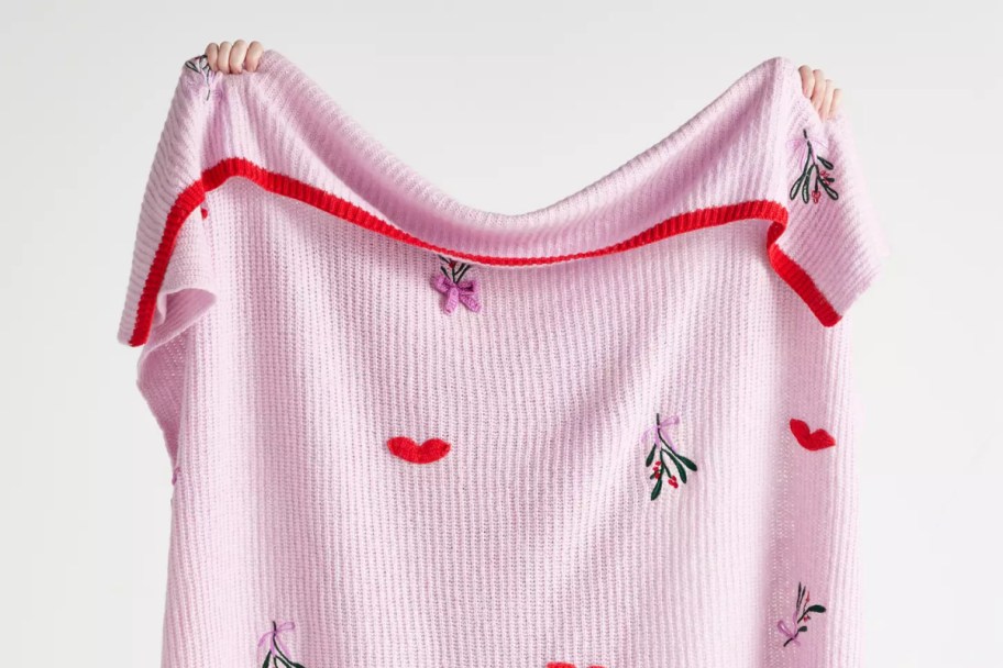 woman holding up a pink knitted blanket with heart and floral decals