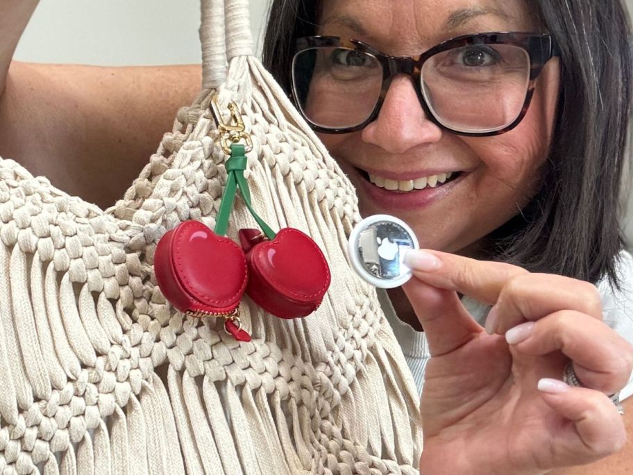 Woman holding an Apple Air Tag next to a bag charm shaped like cherries