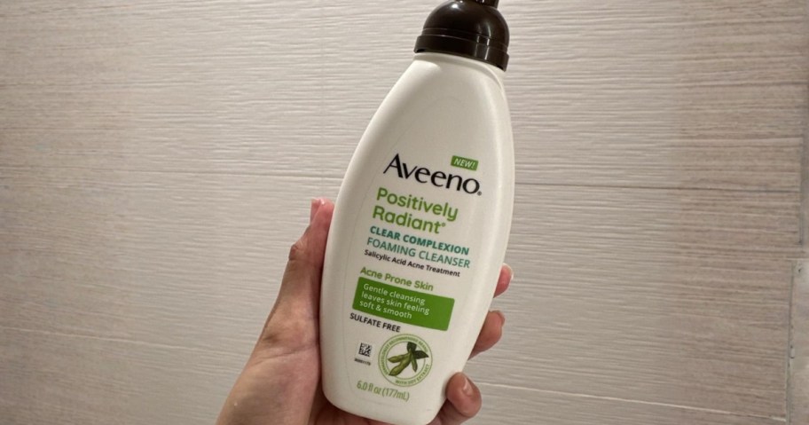Person holding Aveeno Positively Radiant Facial Cleanser in bathroom
