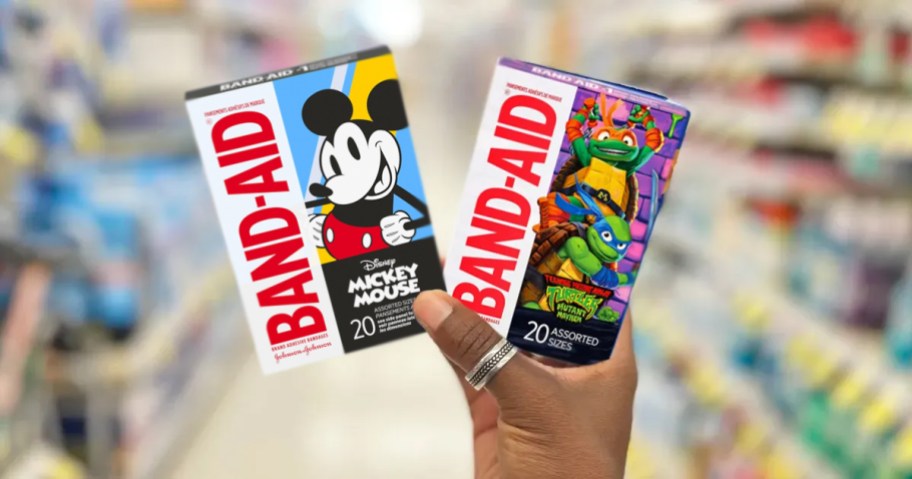 hand holding up two boxes of Band-Aid Bandages in Mickey Mouse and TMNT prints