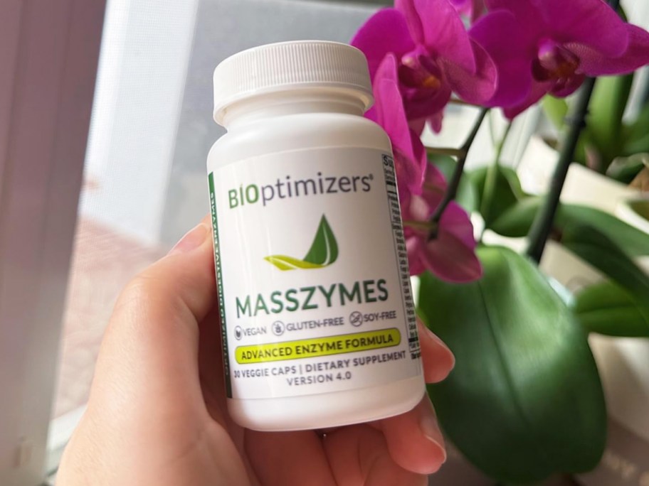 hand holding BiOptimizers MassZymes Supplement bottle near orchid plant