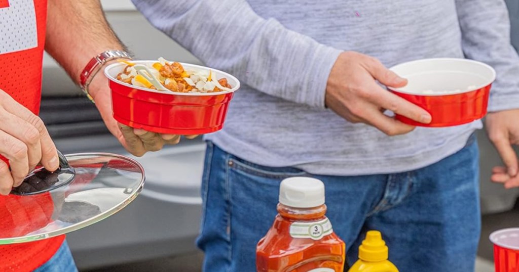 Two men holding red disposable plastic bowls at a football tailgate