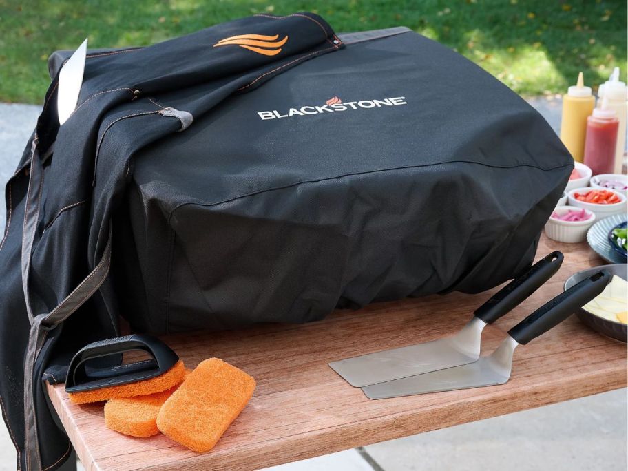 A covered Blackstone Omnivore Griddle with apron scrub pads, and spatulas