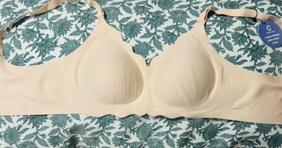A nude-colored bra laid flat on a floral-patterned fabric background.