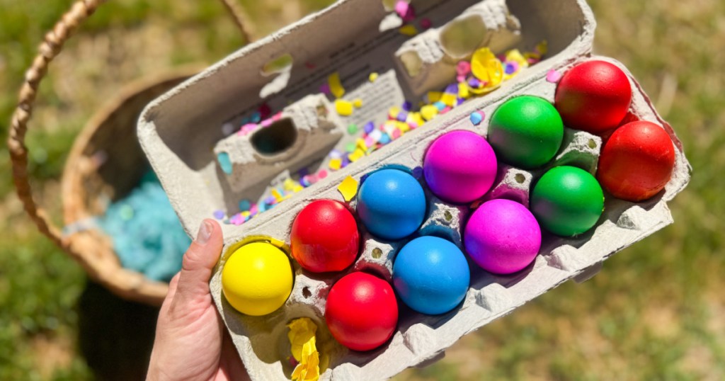 Hand holding up cardboard carton, filled with colorful confetti, Easter eggs