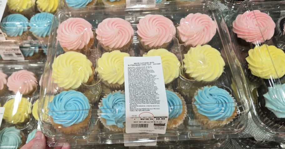 hand holding a tray of pastel frosted cupcakes