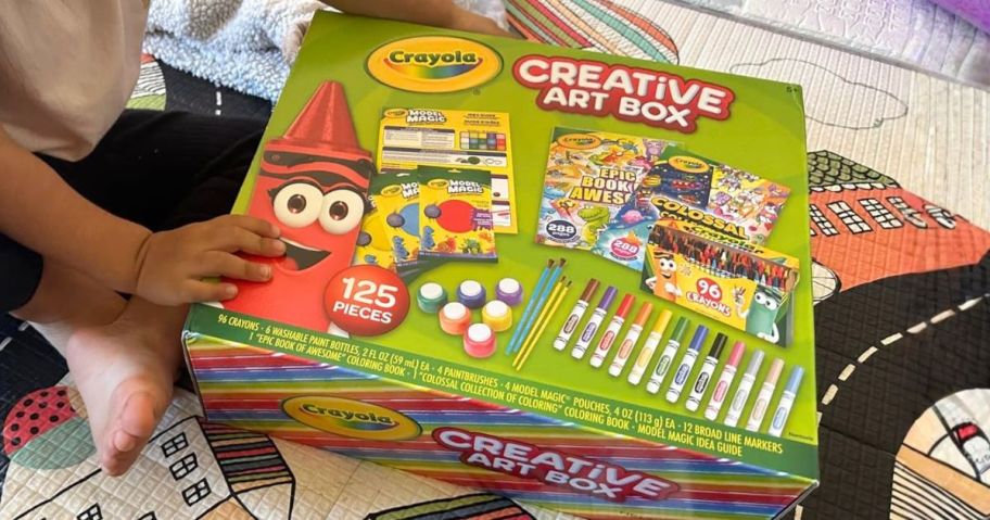 kid holding Crayola Creative Art Box 125-Piece Kids' Set on floor