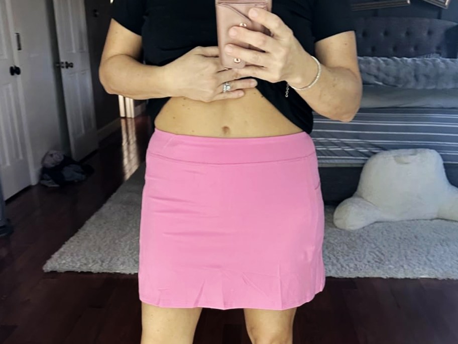 woman taking photo in mirror wearing black top and pink skort