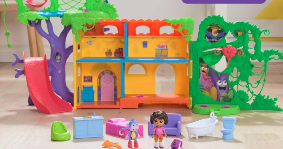 Toy playset featuring a colorful treehouse with a red slide, dolls, and furniture. The set includes a purple couch, bathtub, and toilet.