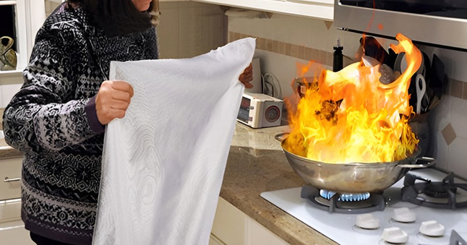woman using a fire blanket on stove fire