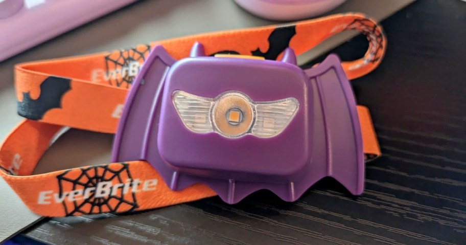 An EverBrite purple bat-shaped kids' Halloween headlamp with an orange strap featuring spiderwebs and bats.