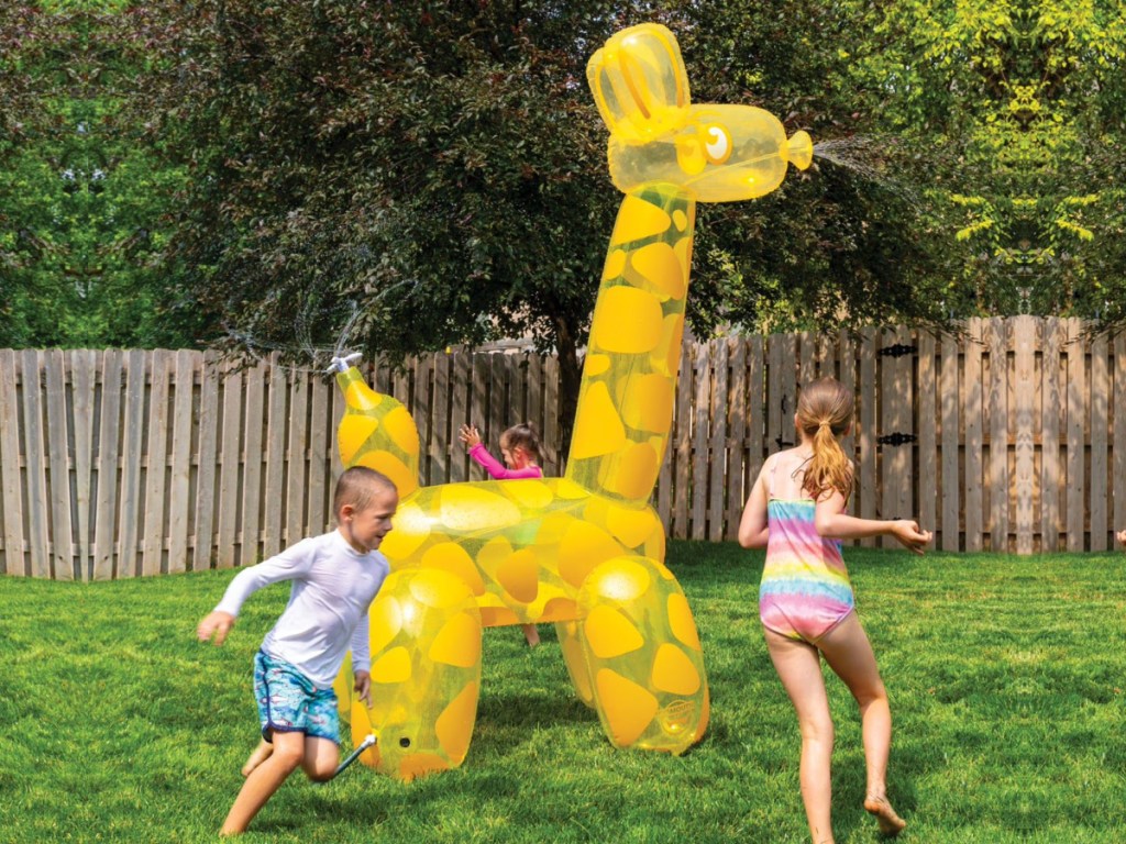 Kids running around a giraffe inflatable sprinkler on the grass