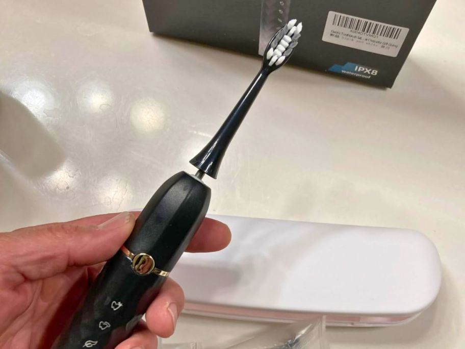 Hand holding Hand holding electric tooth brush with box behind it 