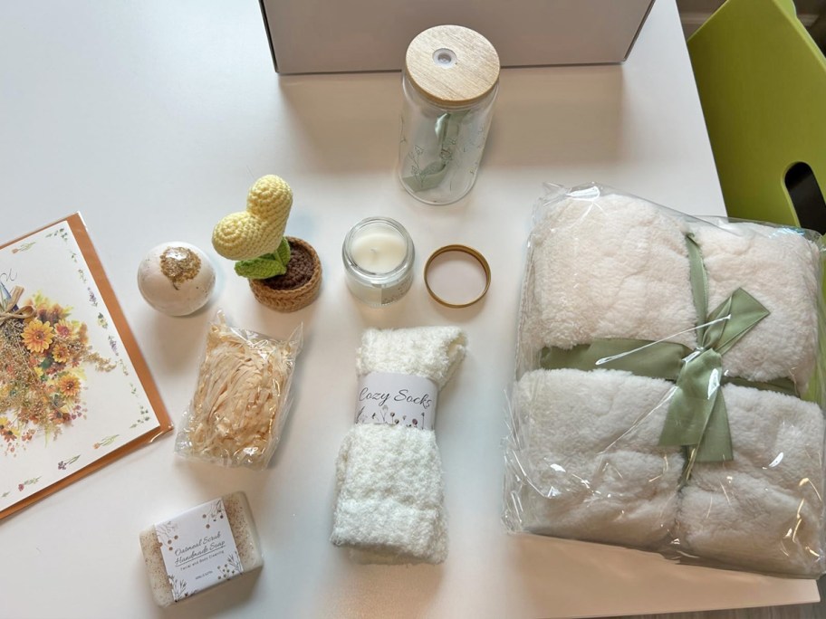 blanket, bath bomb, glass cup, and crochet planter on card near gift box and card