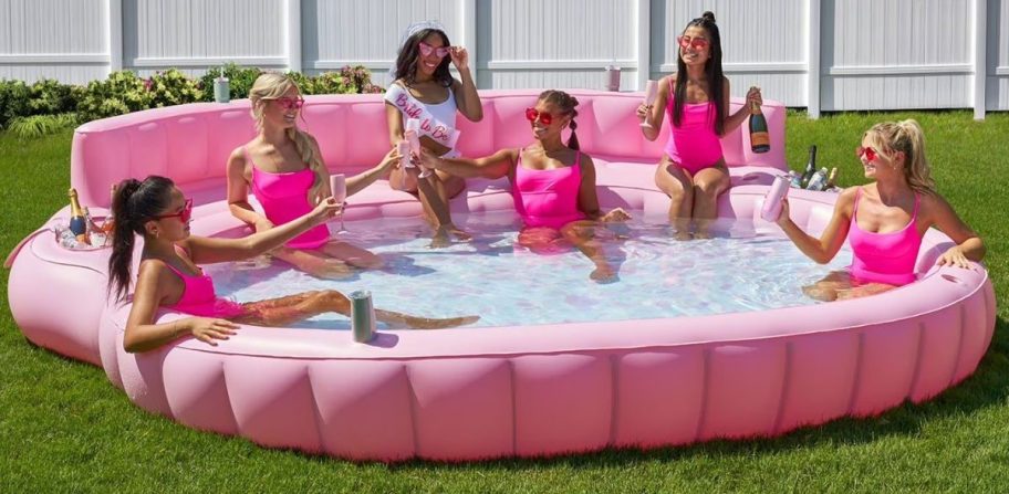 Women laying inside of an oversized pink pool outside