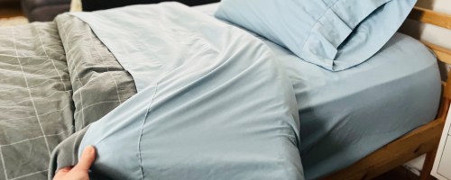 hand holding blue sheet on a bed