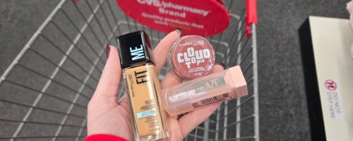 Maybelline cosmetics in a woman's hand over a CVS shopping cart