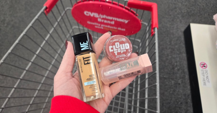 Maybelline cosmetics in a woman's hand over a CVS shopping cart