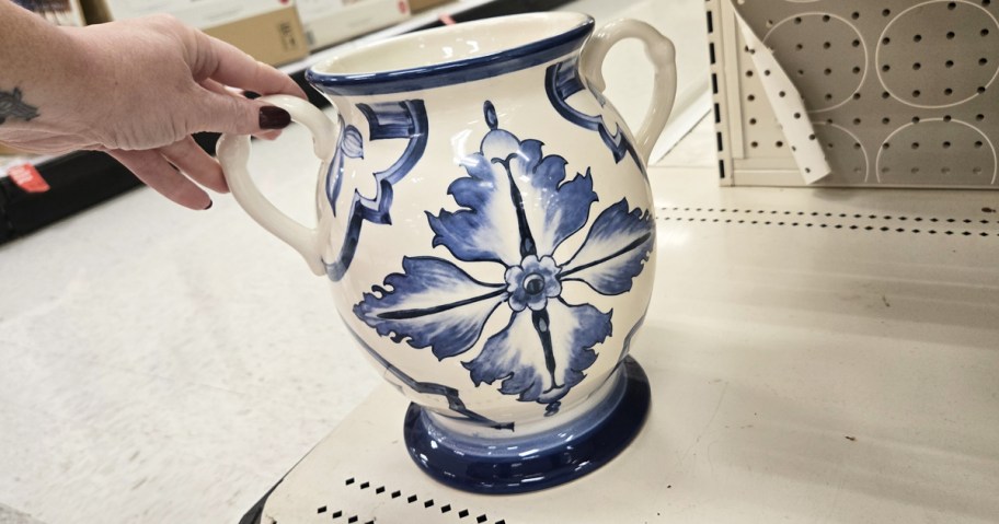 hand touching a blue and white vase on store shelf