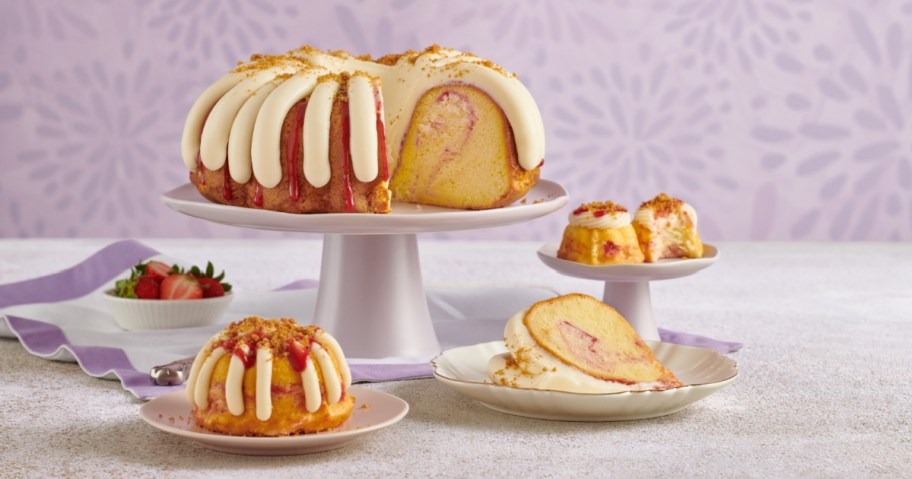 Variety of Nothing Bundt Cakes Strawberry Cheesecake Swirl bundt cakes with a dish of strawberries and a purple ribbon